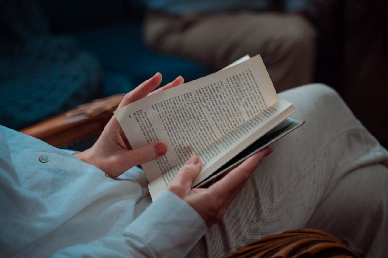 A person leisurely sitting and reading an open book indoors, capturing the essence of relaxation.